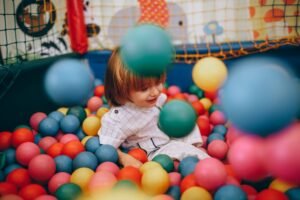 Crianças brincando em parquinho indoor com brinquedos coloridos e estrutura de segurança