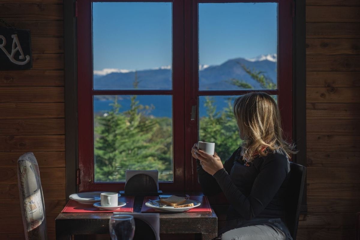 Restaurantes com Vista em Gramado: onde jantar com paisagem 2 Mulher sentada à mesa de restaurante apreciando vista para montanha