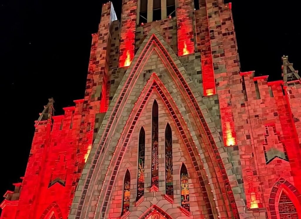Sonho de Natal Canela 2025: Programação Completa 1 Parede da catedral de pedra de Canela iluminada com luzes vermelhas.