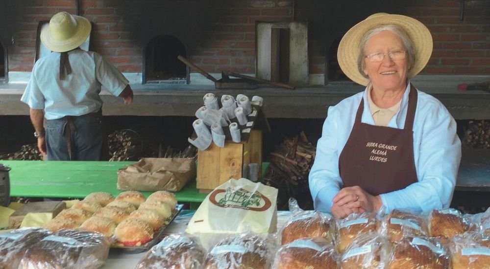 Festa da Colônia de Gramado 2024: Tradições e Sabores 1 Foto na casa do Colono em Gramado, uma senhora vendendo os pães tradicionais em Gramado