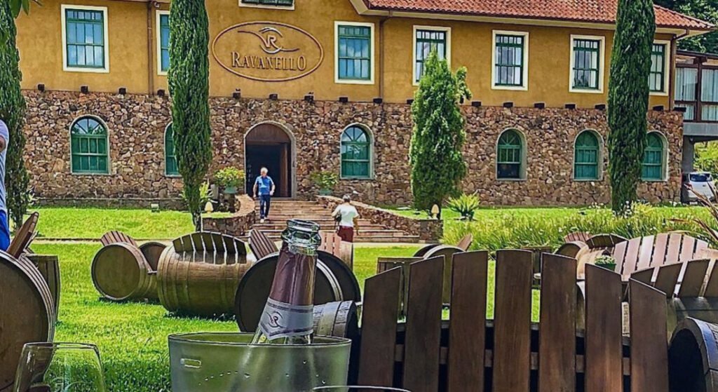 O que fazer em Gramado com chuva? 10 dicas turísticas 6 Vinícola Ravanello com pessoas andando pela entrada, foto tirada da mesa com garrafa de vinho aberta sobre a mesa